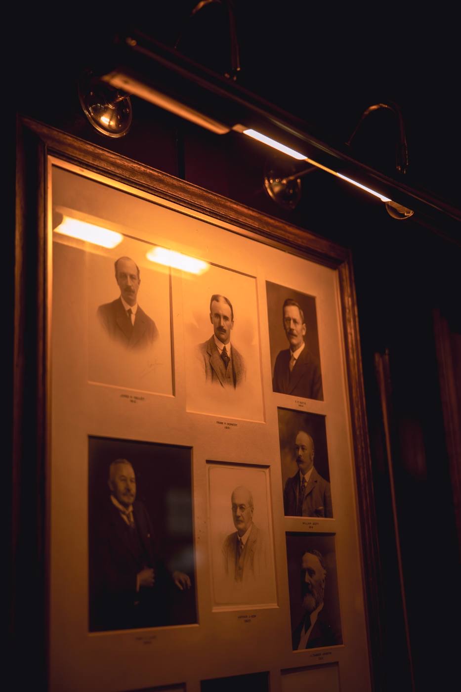 An illuminated wall display of framed sepia portraits of past captains