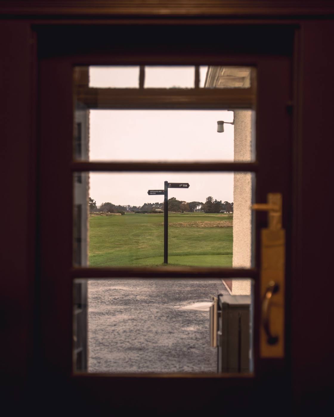 An open clubhouse doorway framing the view out to the fingerpost and the course beyond