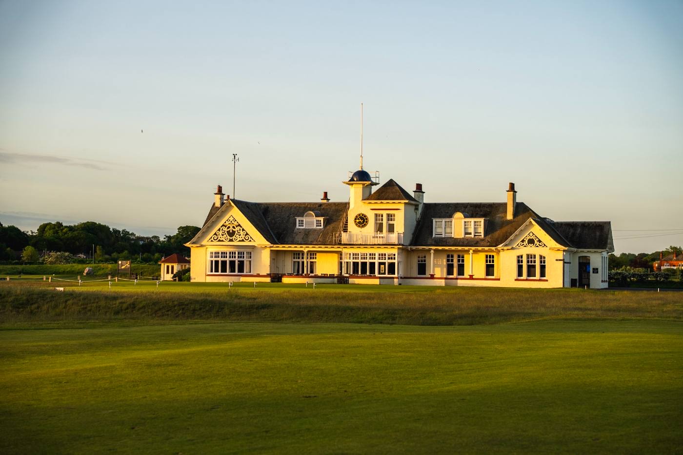 The clubhouse frontage in evening light, the verandah and harled gables lit gold