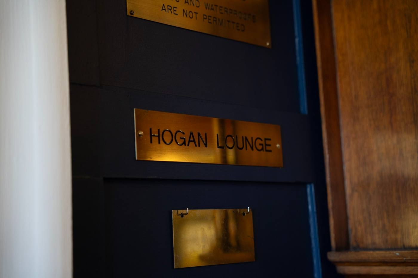A brass door plate engraved HOGAN LOUNGE on a dark panelled wall