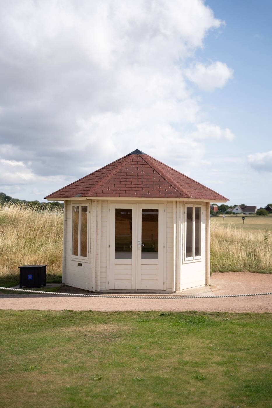 A small white octagonal pavilion with a tiled pitched roof at the edge of the course