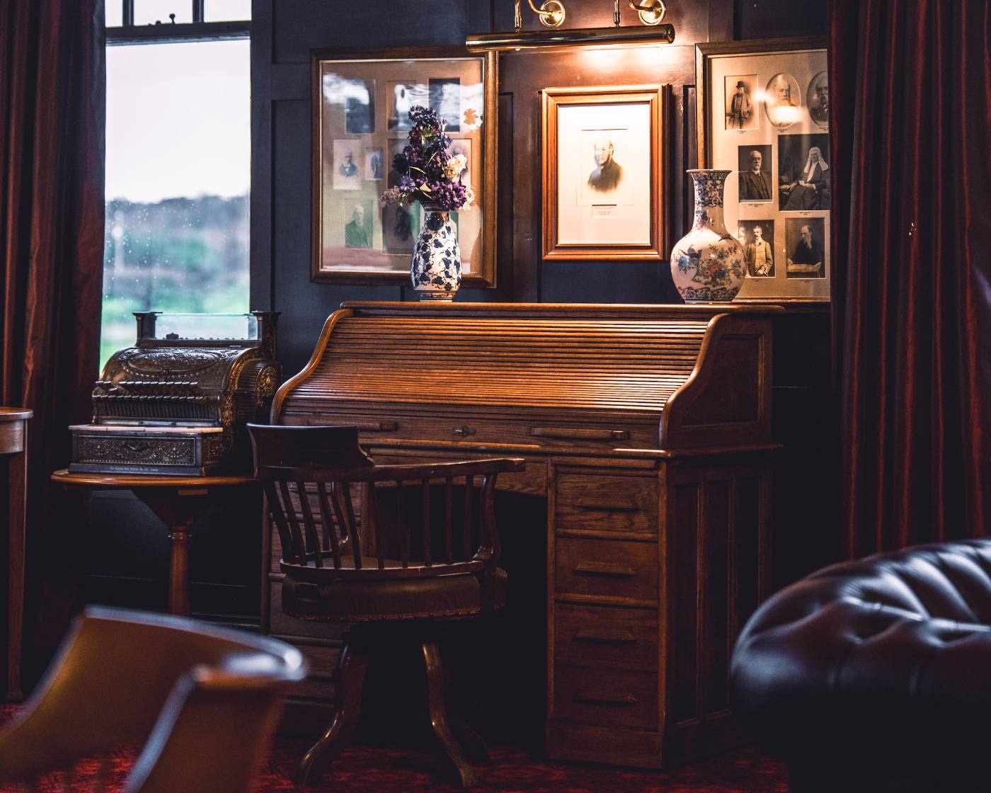 A lounge corner with roll-top desk, brass cash register and a dense framed picture wall