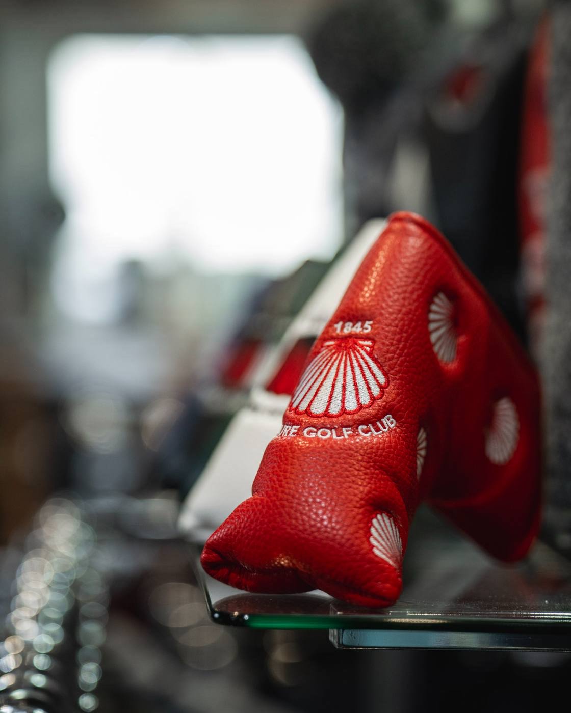 A red leather blade putter cover stamped 1845 with the shell crest