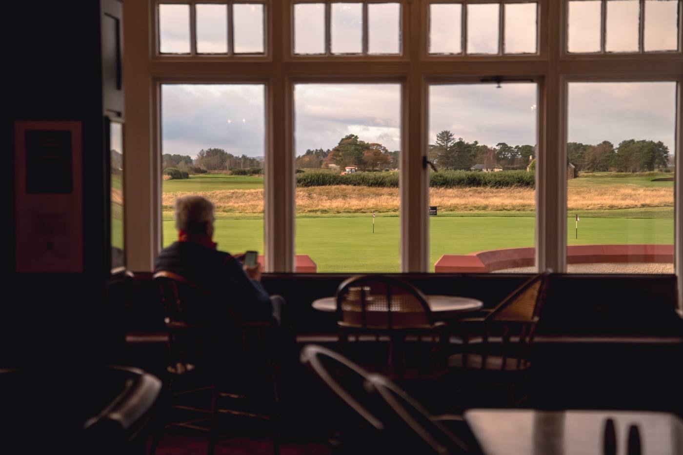 Interior looking out through the clubhouse window wall onto the course, a member seated in silhouette