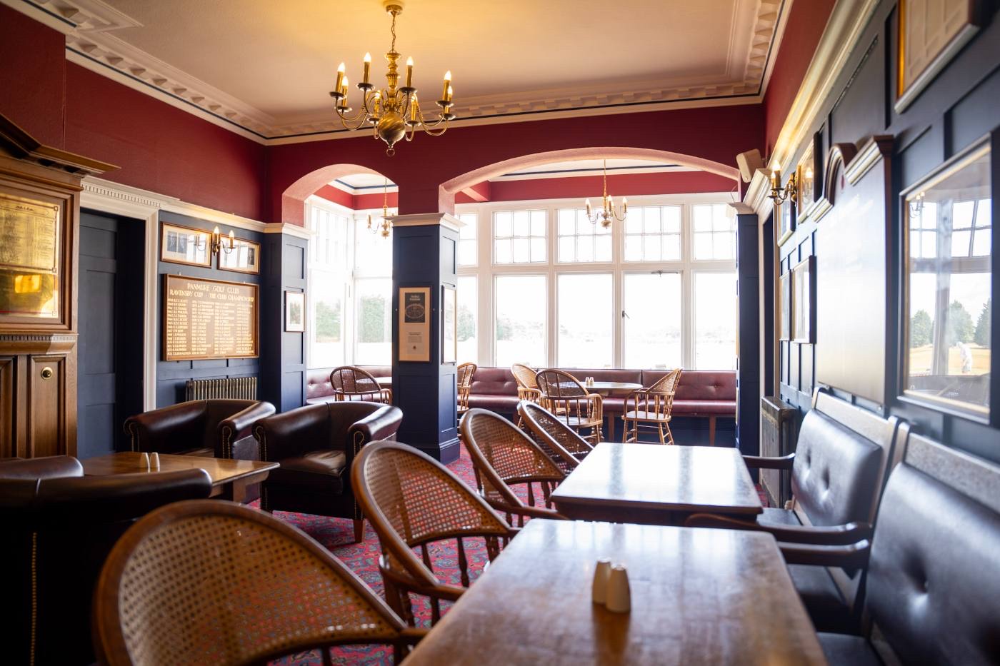 The clubhouse lounge with honours boards, cane chairs and windows onto the course